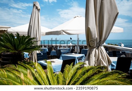 Restaurant or cafe on outdoor terrace with view of see. Tables set with blue linen dishes. Italian style. Tourism and travel. Enjoying life. Beautiful places.
