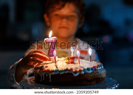 Adorable happy blond little kid boy celebrating his birthday. Child blowing seven candles on homemade baked cake, indoor. Birthday party for school children, family celebration of 7 years Royalty-Free Stock Photo #2359205749