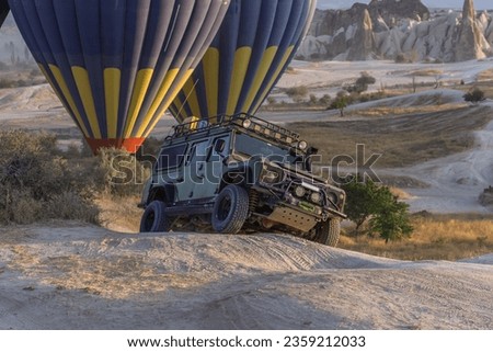 A large, spectacular SUV on safari in the sun. Expedition in a prepared vehicle to incredible places. Big wheels. Travel to Cappadocia. Suspension articulation. Offroad. Balloons on the background.