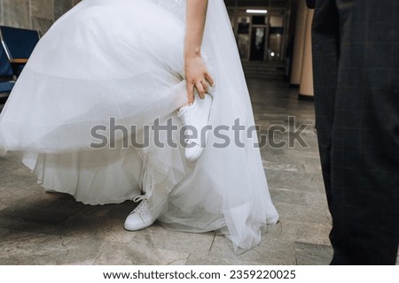 The bride in a white dress puts on, straightens sports sneakers on her feet. Wedding photography, portrait. Royalty-Free Stock Photo #2359220025