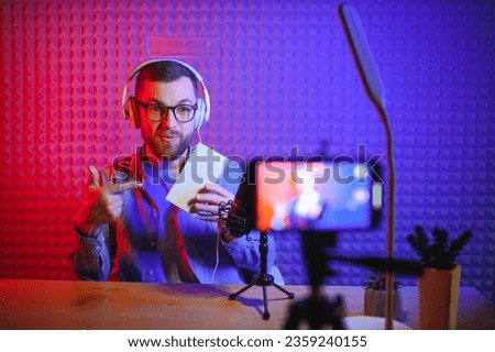 Young male technology blogger recording video blog or vlog about new smartphone and other gadgets at home studio. Blogging, Work from Home concept. Focus on gadgets at the table. Web Banner. Royalty-Free Stock Photo #2359240155