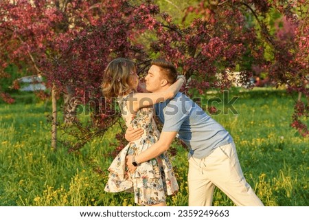 This pic captures a young couple strolling and bustin' out some moves in the park amidst bloomin' trees at sunset. It's all about that fun date vibe, joy, weekend vibes, and outdoor activity.