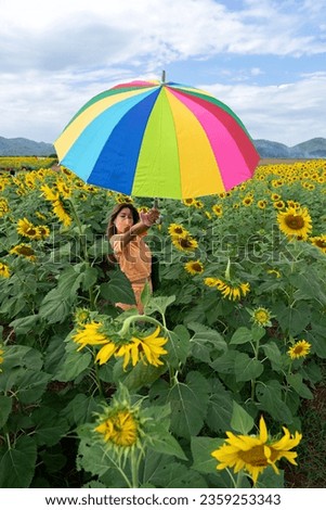 Asian woman holding colorful umbrella in yellow and green sunflower field with blue sky background.