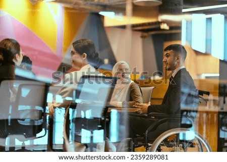 In a modern glass startup office, a wheelchair-bound director leads a successful meeting with colleagues, embodying inclusivity and teamwork. Royalty-Free Stock Photo #2359289081