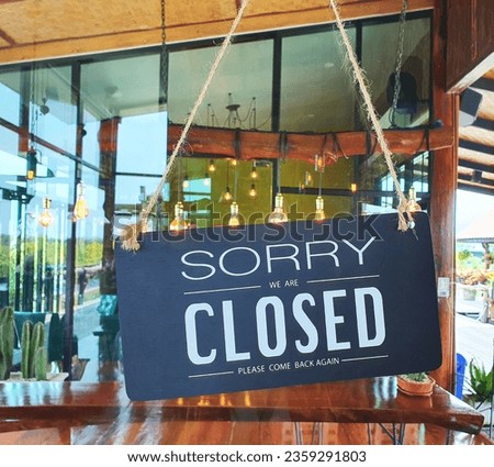 Wooden sign mounted on glass door write a message in white ink "Sorry we are closed please come black again". The sign is installed in front of the restaurant, coffee shops. Text on vintage wooden sig