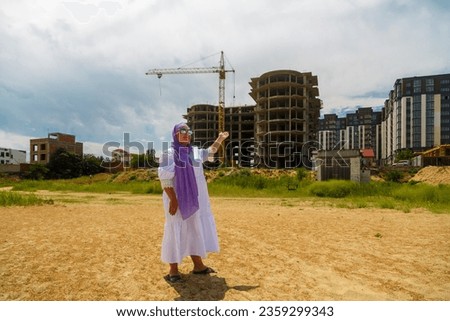 A Muslim woman manager stands at a house under construction with a tower crane and advertises a new complex. Horizontal photo