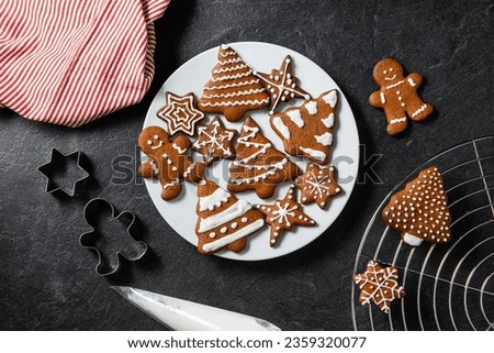christmas baking, cooking and food concept - close up of iced gingerbread cookies on plate, molds, towel and pastry bag on black table top Royalty-Free Stock Photo #2359320077