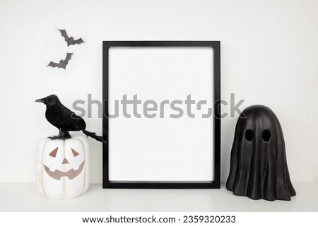Halloween mock up. Black frame on a white shelf with jack o lantern, ghost and crow decor. Portrait frame against a white wall. Copy space.