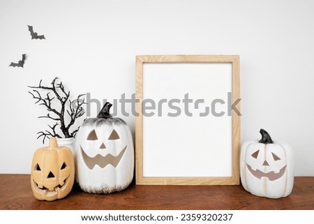 Halloween mock up. Wooden frame on a wood shelf with black branches and jack o lantern decor. Portrait frame against a white wall. Copy space.