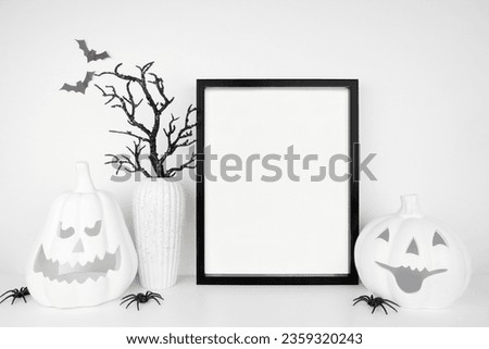 Halloween mock up. Black frame on a white shelf with jack o lanterns and black branch decor. Portrait frame against a white wall. Copy space.