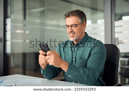 Busy smiling business man executive of mid age looking at smartphone digital technology, older mature businessman entrepreneur investor using cell phone working on mobile cellphone in office.