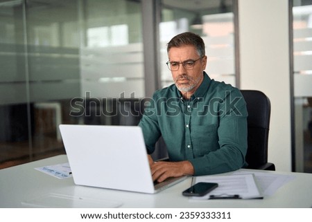 Busy middle aged professional business man executive investor using computer working at desk. Male manager expert looking at laptop thinking on online finance market analysis, elearning in office. Royalty-Free Stock Photo #2359333311