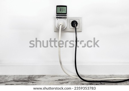 White double outlet installed on the white wall with inserted timer socket and a black electrical plug, front view. Royalty-Free Stock Photo #2359353783