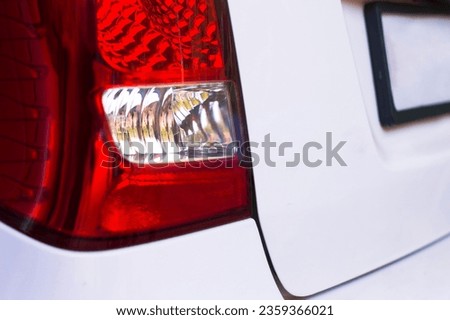 Close-up of a red tail light on a car. The light is in the shape of a rectangle with rounded corners. It has a red lens and a white reflector.