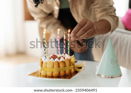 Selective focus, closeup African American woman, birthday girl blowing out candle on birthday cake, making wish while standing at home in living room. Celebration concept