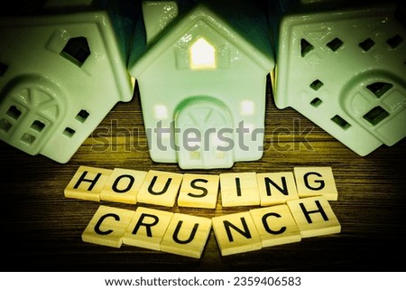 Housing crunch i wooden letters and ceramic houses leaning against each other, one house with lights
