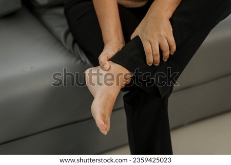 Elderly asian woman sitting on the couch, foot pain.
