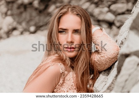 Woman summer travel sea. Happy tourist in beige dress enjoy taking picture outdoors for memories. Woman traveler posing on the beach surrounded by volcanic mountains, sharing travel adventure journey