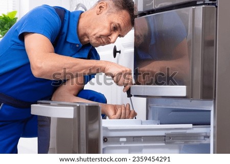 Mature Male Serviceman Repairing Refrigerator With Toolbox In  Kitchen Royalty-Free Stock Photo #2359454291