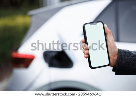 Process of charging is showing on smartphone. Close up view of man with his electric car. Man holding smartphone while charging car at electric vehicle charging station, closeup.