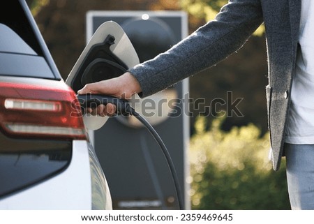 The driver of the electric car inserts the electrical connector to charge the batteries. Unrecognizable man attaching power cable to electric car. Electric vehicle Recharging battery charging port. Royalty-Free Stock Photo #2359469645