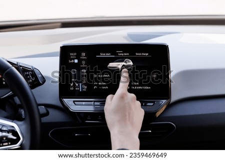 Male finger using an intelligent multimedia touchscreen system for modern electric automobiles. Green energy, zero-emission car interior view. Long-range electric vehicle. Royalty-Free Stock Photo #2359469649