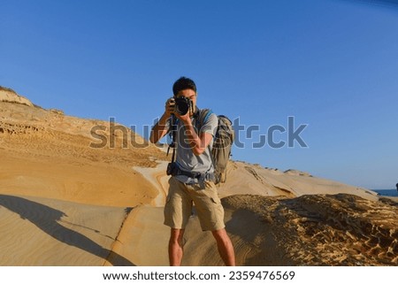 A young man travelling on stony area. Landscape  photographer  with the camera in his hands walking on rocky terrain and wearing backpack