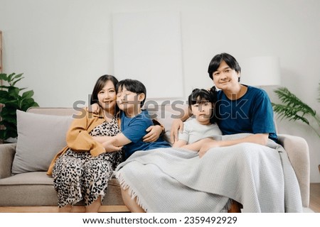 Asian Overjoyed kids sitting on sofa with cheerful parents, watching funny video on computer. Happy married couple enjoying spending weekend time with children, looking at laptop and tablet 