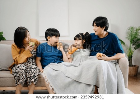 Asian Overjoyed kids sitting on sofa with cheerful parents, watching funny video on computer. Happy married couple enjoying spending weekend time with children, looking at laptop and tablet  Royalty-Free Stock Photo #2359492931