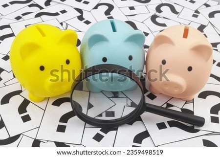 Three piggy banks under magnifying glass on question marks background.