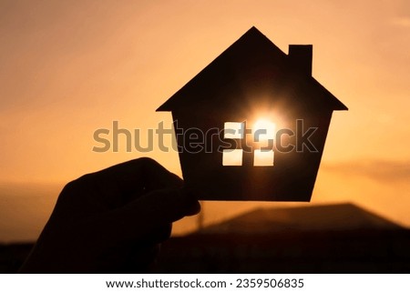 Hands holding paper house on sunset sky, family home, homeless housing, and home protection insurance concept, international day of families, new life, foster home care, and real estate. Royalty-Free Stock Photo #2359506835