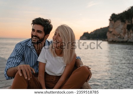 Delightful couple sitting at the beach. Two smiling people man and woman looking aside and laughing while having a fun at the sea dock.