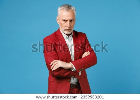 Displeased dissatisfied elderly gray-haired mustache bearded business man wearing red jacket suit standing holding hands crossed looking camera isolated on blue color wall background studio portrait Royalty-Free Stock Photo #2359533201