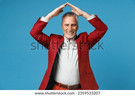Smiling funny elderly gray-haired mustache bearded business man in red jacket suit standing hold hands above head like roof of house looking camera isolated on blue color background studio portrait Royalty-Free Stock Photo #2359533207