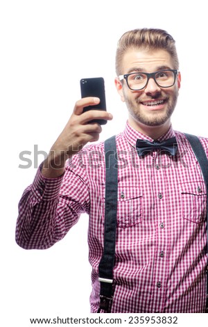 Young handsome smiling caucasian man with beard and bow tie holding his smartphone and looking at camera in good mood isolated on white background.
