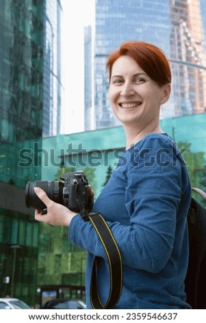 Vertical portrait of a woman with a camera. An urban photographer photographs modern architecture. The woman smiles and looks at the camera.