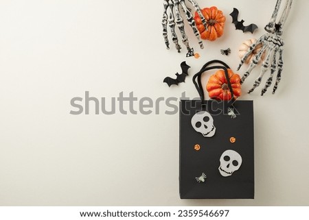 Surprising loved ones with Halloween treats. Top view shot of  black paper gift bag, spooky skeleton hands, pumpkins, scary silhouettes, confetti on light grey background with ad space