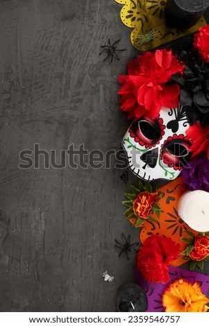 Pay tribute to mexican tradition at the grand Day of the Dead festival. Top view vertical shot of carnival mask, flowers, colorful garland, candles, scary decor on texture grey background with ad zone
