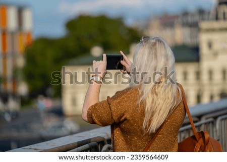 Tourist blonde woman taking pictures of navy ships from the bridge in Riga, Latvia