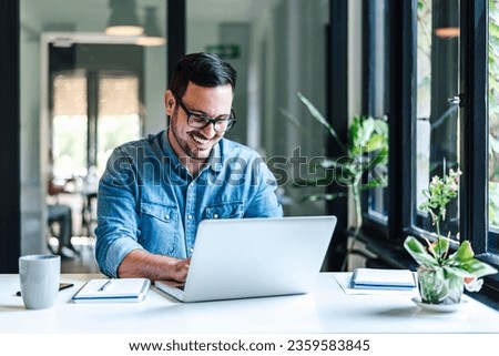 Smiling young entrepreneur working on laptop at table. Confident male professional is analyzing success plan. He is sitting at home office. Royalty-Free Stock Photo #2359583845