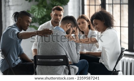 Diverse people sit in circle participate in group psychological session, touch support upset friend, multiracial colleagues comfort unhappy stressed male suffering from mental addiction problems Royalty-Free Stock Photo #2359587241