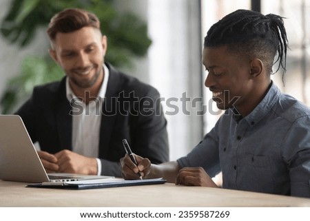 Excited african American male employee sign paper document close deal after office interview, happy biracial man worker client put signature on contract, make agreement at meeting, employment concept