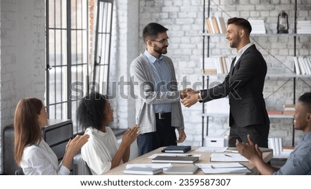 Young Caucasian boss shake hand of male employee, congratulate with job promotion at meeting, confident businessman handshake worker, greeting with employment, get acquainted at team briefing Royalty-Free Stock Photo #2359587307