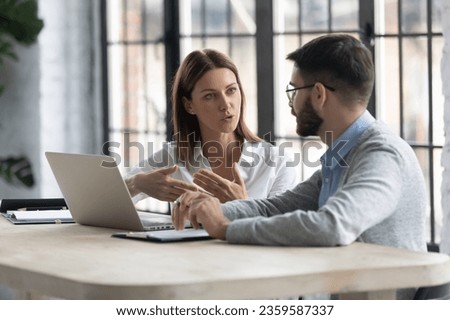 Concentrated diverse businesspeople sit at desk talk brainstorm at office meeting using laptop, focused colleagues consider discuss business ideas, work at computer at briefing, collaboration concept Royalty-Free Stock Photo #2359587337