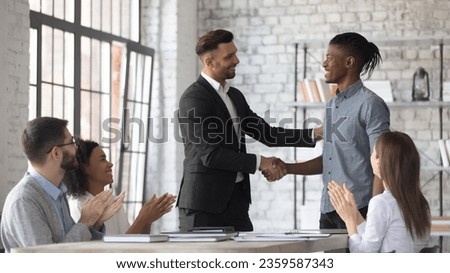 Smiling Caucasian businessman shake hand congratulate with good work achievement result african American male employee, boss handshake greeting with promotion excited biracial worker at meeting Royalty-Free Stock Photo #2359587343
