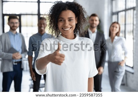 Smiling young african American female leader stand forefront show thumb up recommend good company service, happy woman employee give recommendation advice to training or course, success concept Royalty-Free Stock Photo #2359587355