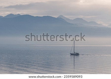 Sailboat sailing on a lake Leman with mountain scenery on a misty day.