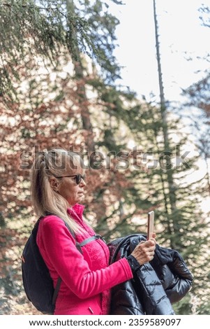 Mature woman taking photos of the natural landscape with her mobile phone while exploring.