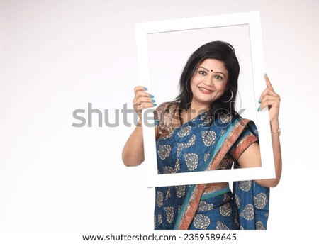 Smiling Attractive Beautiful Indian happy Woman holding photo frame shaped white carboard while standing isolated in white background.