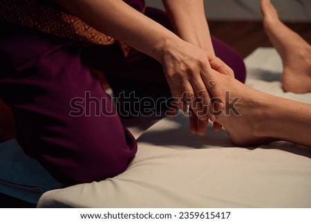 Qualified masseuse giving traditional Thai feet massage to her client Royalty-Free Stock Photo #2359615417